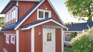 Et rødt hus med hvid dør og vinduer, en lille veranda og en have med hvide blomster.