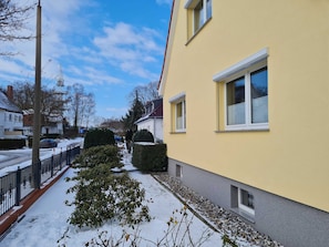 Ein Wohngebäude mit gelber Fassade, einem gepflasterten Weg und verschneitem Grund.
