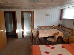 A room with a dining table, chairs, a sofa, a bed, and a window with curtains. - Apartment in Ahlbeck - Apartment (basement up to 3 pers.) (Heringsdorf)