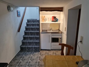 Eine kompakte Küche mit eingebautem Ofen, Mikrowelle und Spüle, ein kleiner Essbereich mit Tisch sowie eine Treppe, die zu einer weiteren Ebene führt.