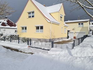 Ein gelbes, zweistöckiges Haus mit einem schneebedeckten Dach und einem schwarzen Metallzaun.