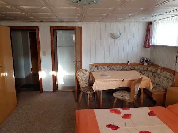 Ein Zimmer mit Esstisch, Stühlen, einer Couch, einem Bett und einem Fenster mit Vorhängen.