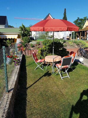 Eine Terrasse mit Tisch und Stühlen, einem roten Sonnenschirm und einem Garten mit verschiedenen Pflanzen und Blumen.