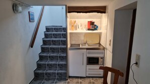 A compact kitchen with a built-in oven, microwave, and sink, a small dining area with a table, and a staircase leading to another level. - Apartment in Ahlbeck - Apartment (basement up to 3 pers.) (Heringsdorf)