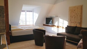 A loft-style bedroom with a large bed, a TV mounted on a wooden beam, and a wooden door. - Cozy apartment in Thulendorf/Sagerheide (Thulendorf/Sagerheide)