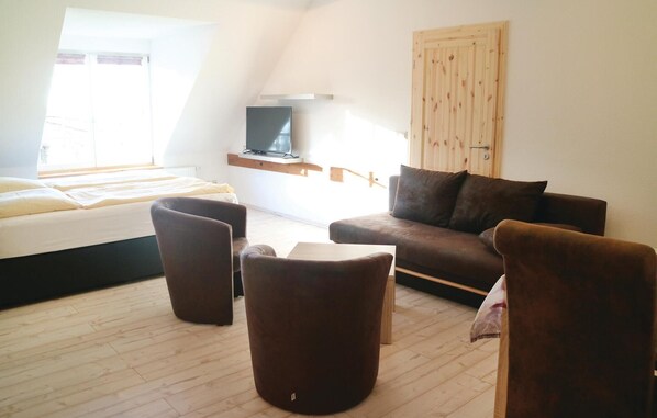 Une pièce moderne et bien éclairée, avec un lit, un canapé marron, deux fauteuils marrons et un téléviseur posé sur une étagère en bois.