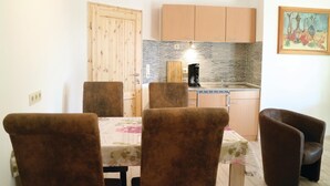 A dining area with a table and chairs, a kitchen with a coffee maker, and wooden cabinets. - Cozy apartment in Thulendorf/Sagerheide (Thulendorf/Sagerheide)