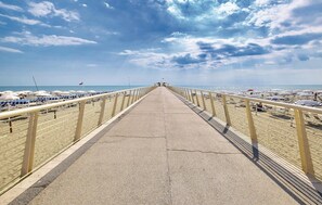 A long, straight concrete walkway with railings on both sides, leading to a beach with umbrellas and lounge chairs. - Stunning apartment in Camaiore (Camaiore)