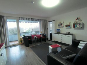 A modern living room with a black leather sofa, a dining table with a red tablecloth, and a kitchen area with white cabinets and a countertop. - Uns Paddemang Dea, Germany (Büsum)