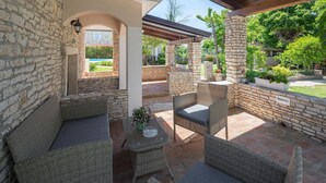 Un patio couvert aménagé avec des meubles en osier, des murs en pierre et une vue sur une piscine.