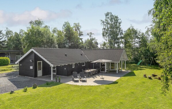 A modern building with a tiled roof, a covered patio with outdoor seating, and a grassy yard. - Nice home in Væggerløse with sauna (Væggerløse)