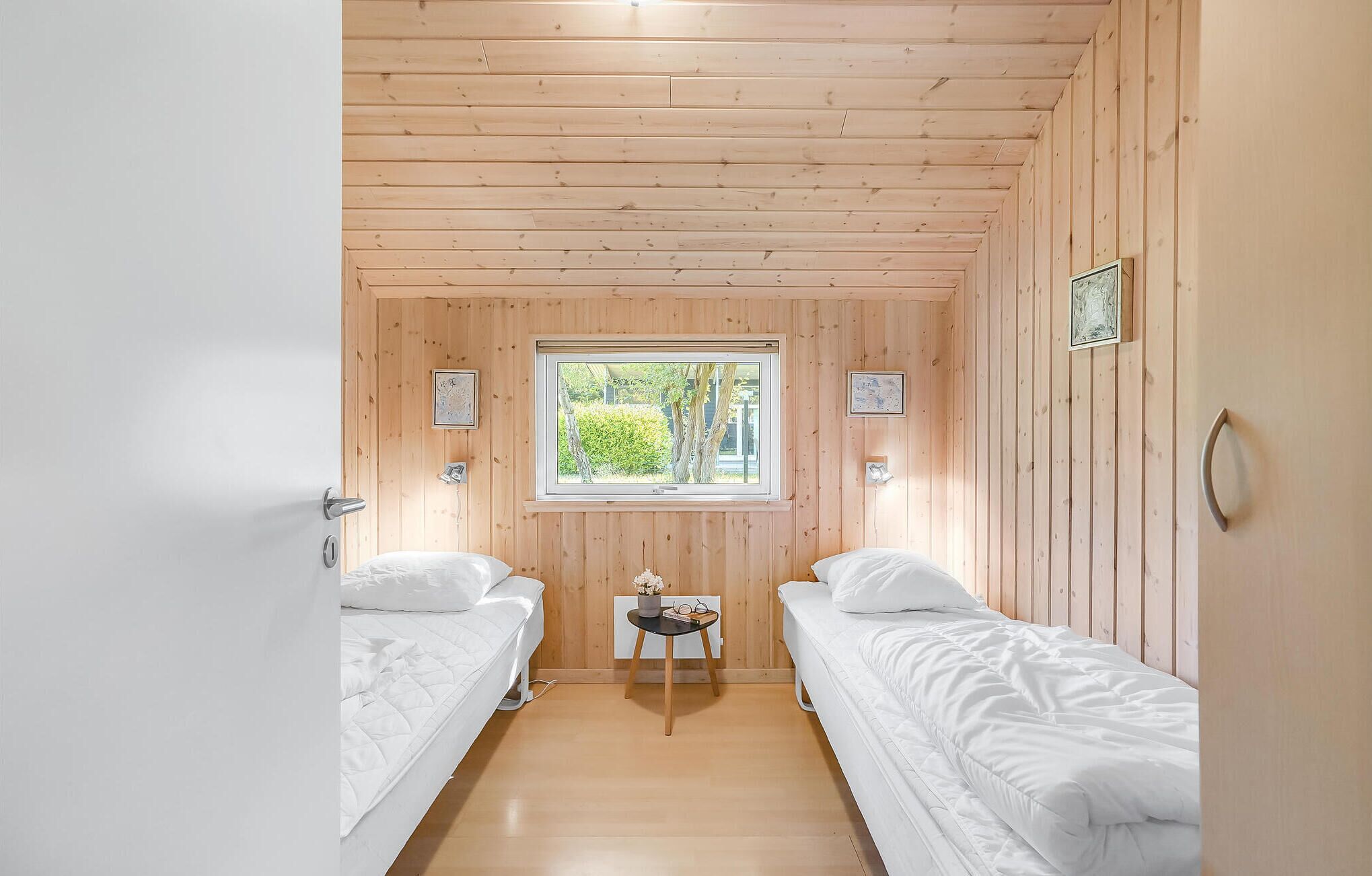 Une chambre avec deux lits simples, une petite table avec un vase et des verres, et une fenêtre donnant sur un paysage verdoyant.