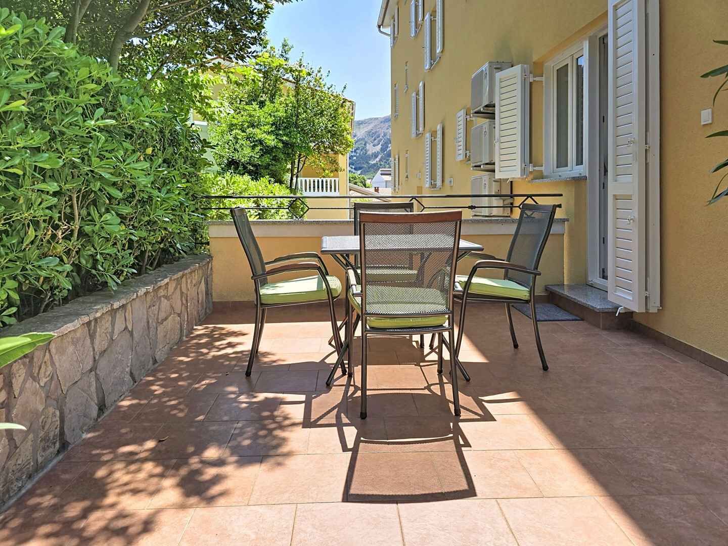 An outdoor patio with a table and chairs, surrounded by stone walls and greenery.
