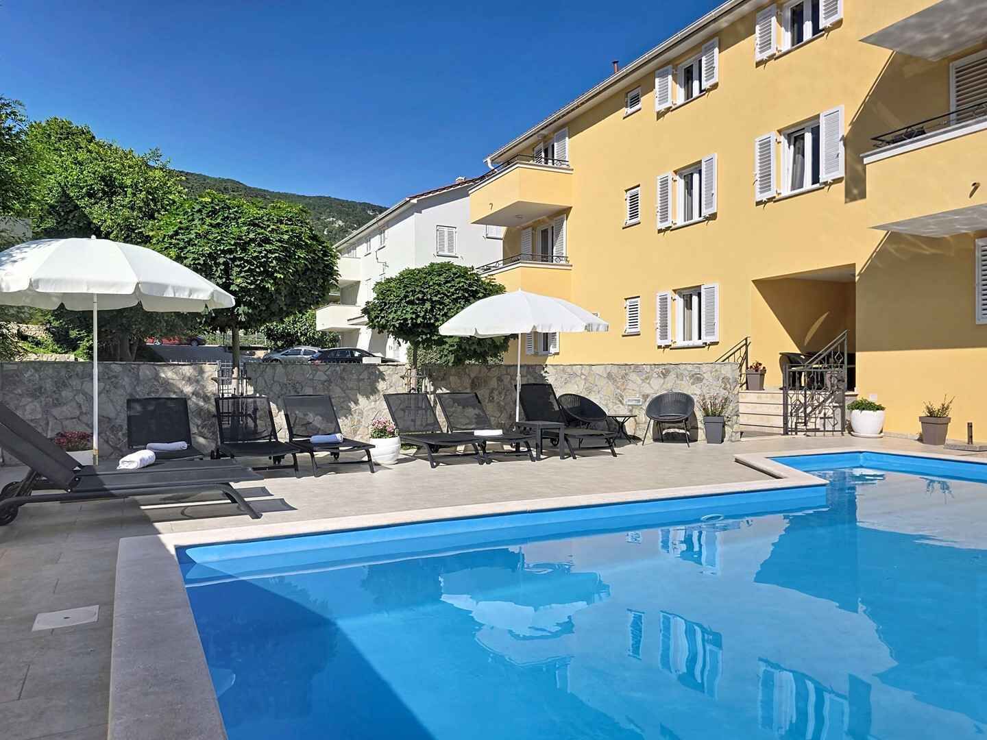 Un espace piscine avec des chaises longues et des parasols, un mur en pierre et un bâtiment jaune doté de fenêtres.
