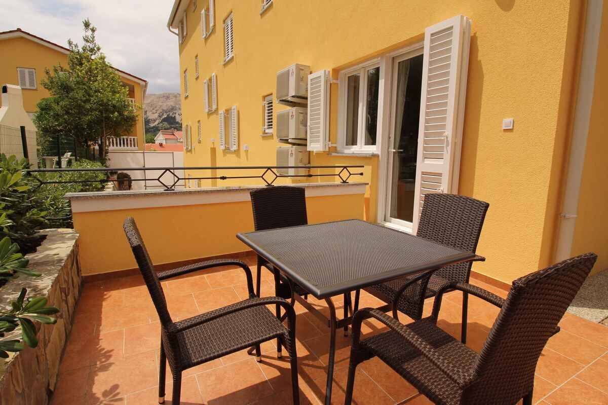 A patio with a table and chairs, a yellow building with shutters, and a view of the surrounding area.