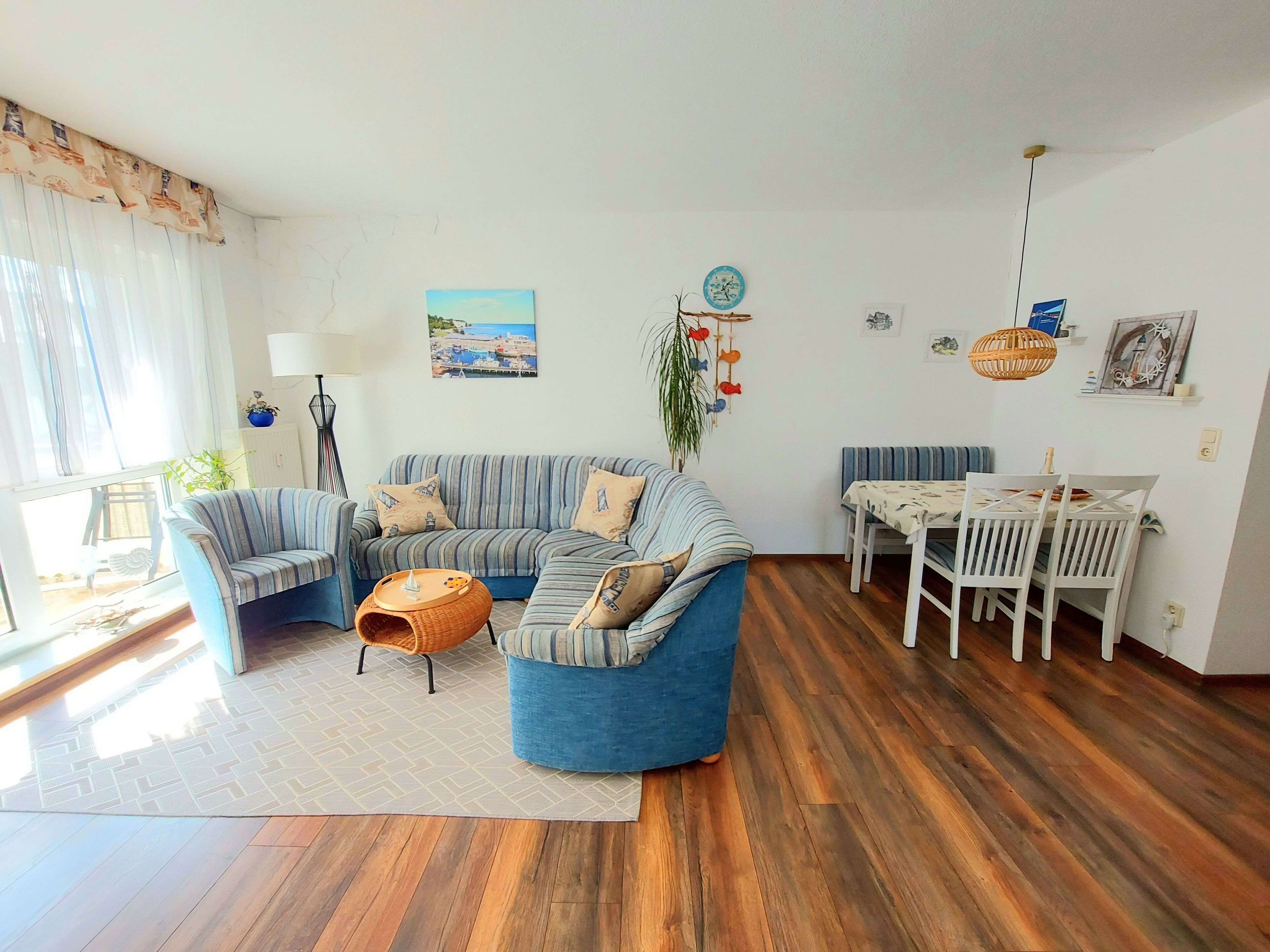 A living room with a sofa set, a dining table with chairs, and a large window with curtains.