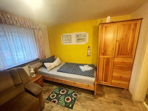 Ein kleiner, gemütlicher Raum mit einem Einzelbett, einem Holzschrank, einem Tisch und einem Stuhl.