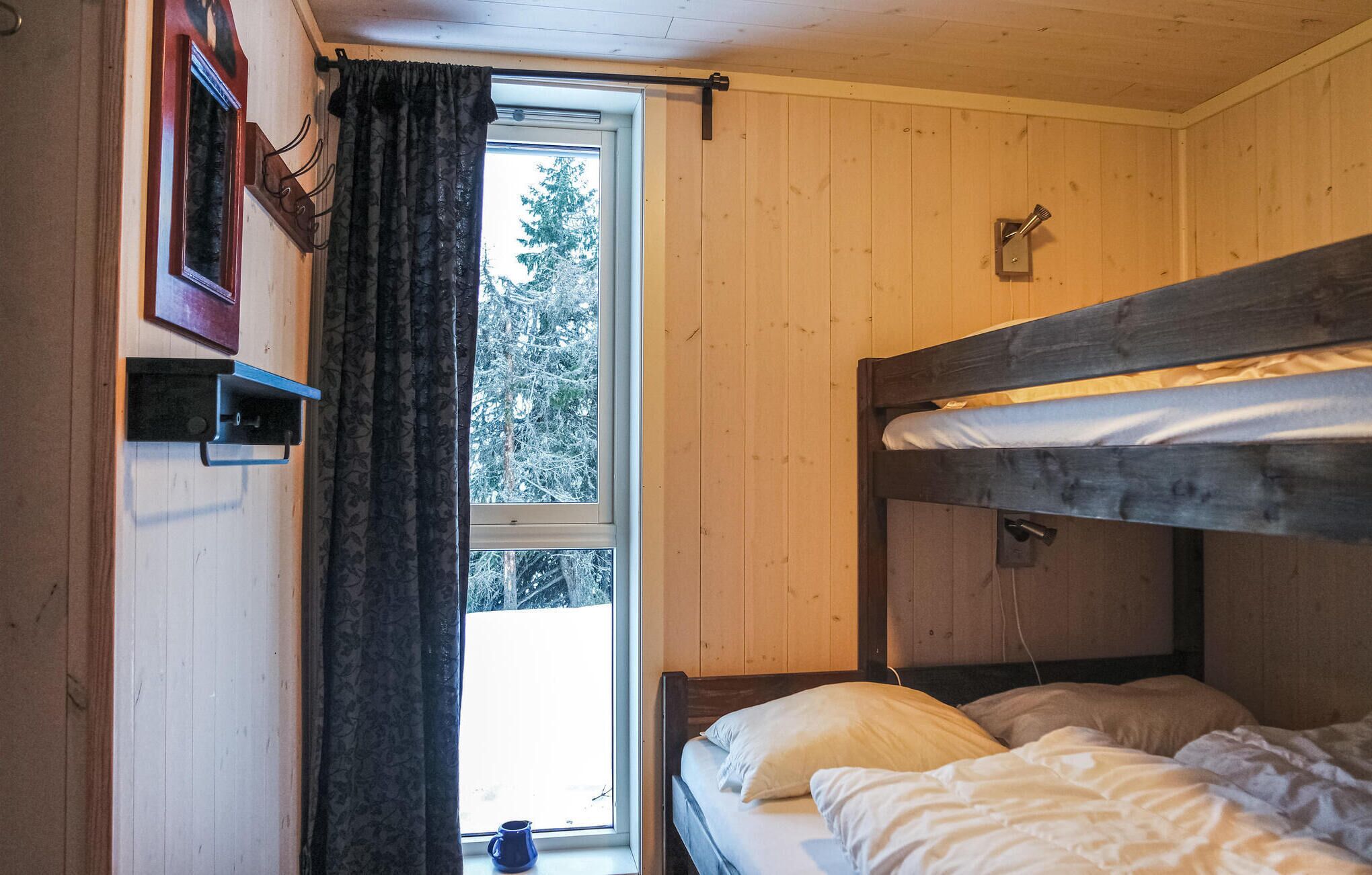 Une pièce de cabane en bois avec des lits superposés, une fenêtre avec des rideaux et une étagère fixée au mur.