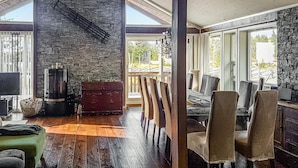 Un vaste espace de vie agrémenté d’une cheminée en pierre, de parquet et de grandes fenêtres offrant une vue sur l’extérieur.
