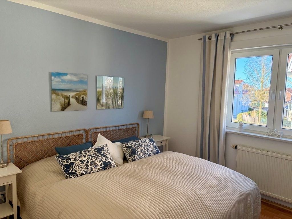 Een slaapkamer met een groot bed, twee nachtkastjes, een raam met gordijnen en twee decoratieve wandobjecten.