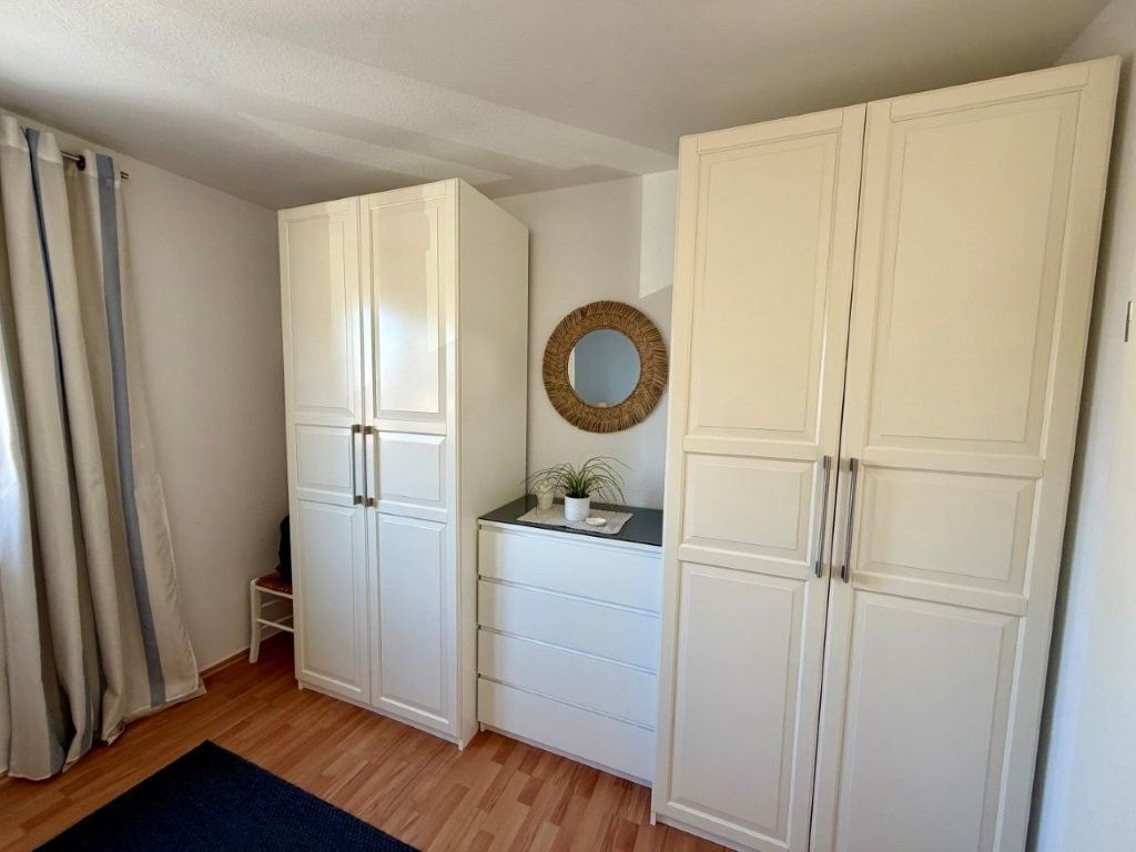 A room with white wardrobes, a small table with a plant, a mirror on the wall, and a blue rug.