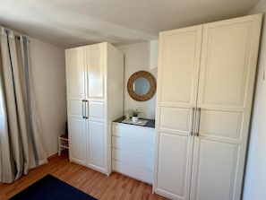 Une pièce avec des armoires blanches, une petite table sur laquelle est posée une plante, un miroir au mur et un tapis bleu.
