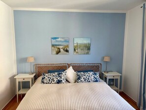 Une chambre à coucher comprenant un lit, deux tables de chevet, une lampe sur chacune, et deux œuvres d’art murales.