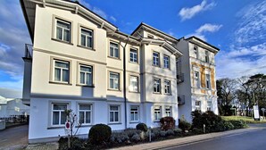 Un edificio residencial de varios pisos con fachada simétrica, numerosas ventanas y un jardín bien cuidado.