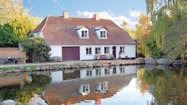 Et hus med tegltag, garage og en sø foran.