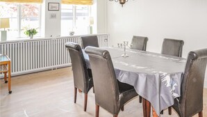 Spiseplads med et rundt bord, seks stole, en lysekrone og en radiator.