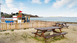 Ein Picknickbereich am Strand mit Holzbänken und einem Spielplatz mit einer roten Flagge.