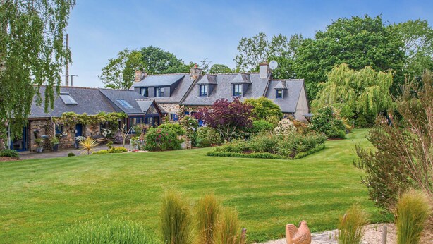 Uma casa grande com vários quartos, um gramado bem cuidado e diversas plantas de jardim.