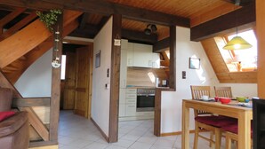 A cozy attic room with a wooden ceiling, a dining area with a table and chairs, and a kitchen in the background.