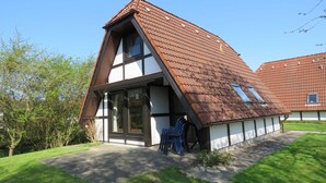 A two-story house with a steeply pitched roof, large windows, and a small garden area with a lawn and a few trees.