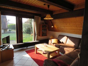 A cozy living room with a wooden ceiling, a red rug, a wooden coffee table, a brown leather sofa, and a television on a stand.