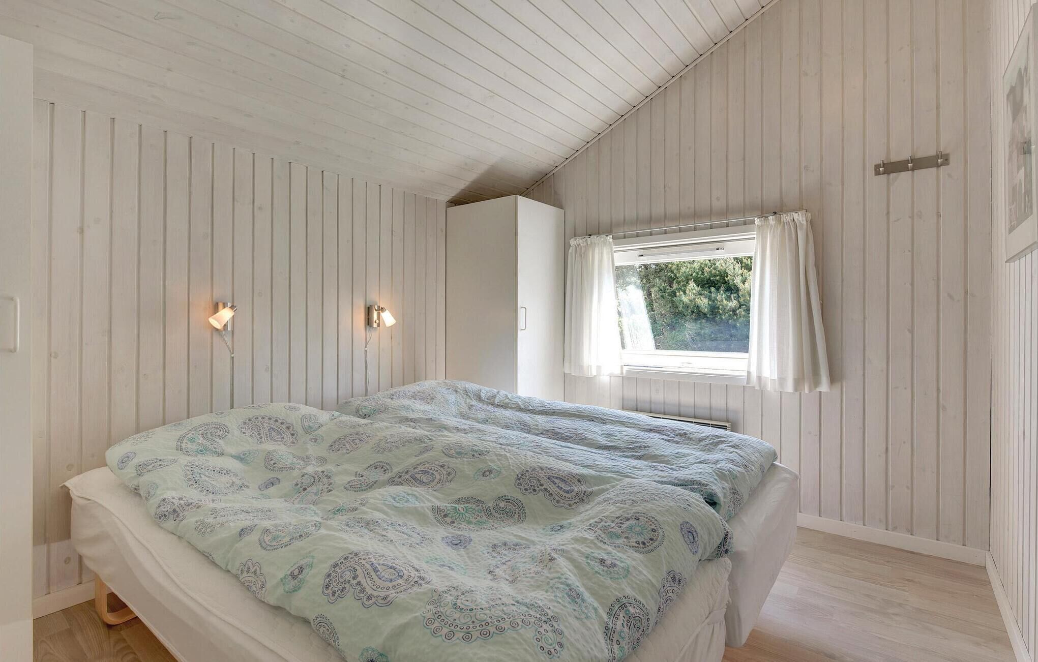 A bedroom with a bed, a window with curtains, and wall-mounted lights.