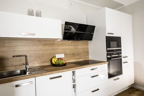 A modern kitchen with white cabinets, a wooden countertop, a built-in oven, and a wall-mounted TV. - Apartment 1 - Villa Starfish - near the beach (Heringsdorf)