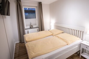 A bedroom with a double bed, a bedside table with a lamp, a window with curtains, and a radiator. - Apartment 1 - Villa Starfish - near the beach (Heringsdorf)