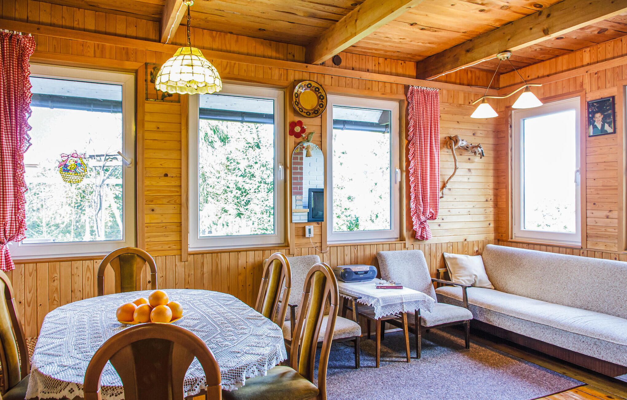 Un acogedor interior de cabaña con paredes de madera, una mesa de comedor con mantel de encaje, un sofá y dos sillones.