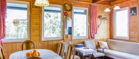 Un acogedor interior de cabaña con paredes de madera, una mesa de comedor con mantel de encaje, un sofá y dos sillones.