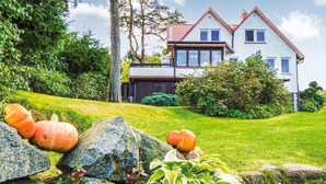 Une maison à deux étages avec un toit rouge, entourée d’une pelouse bien entretenue et de gros rochers.