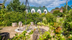 Un jardin agrémenté d’une structure métallique, de souches d’arbres et, au fond, d’une maison dotée d’un toit végétalisé.