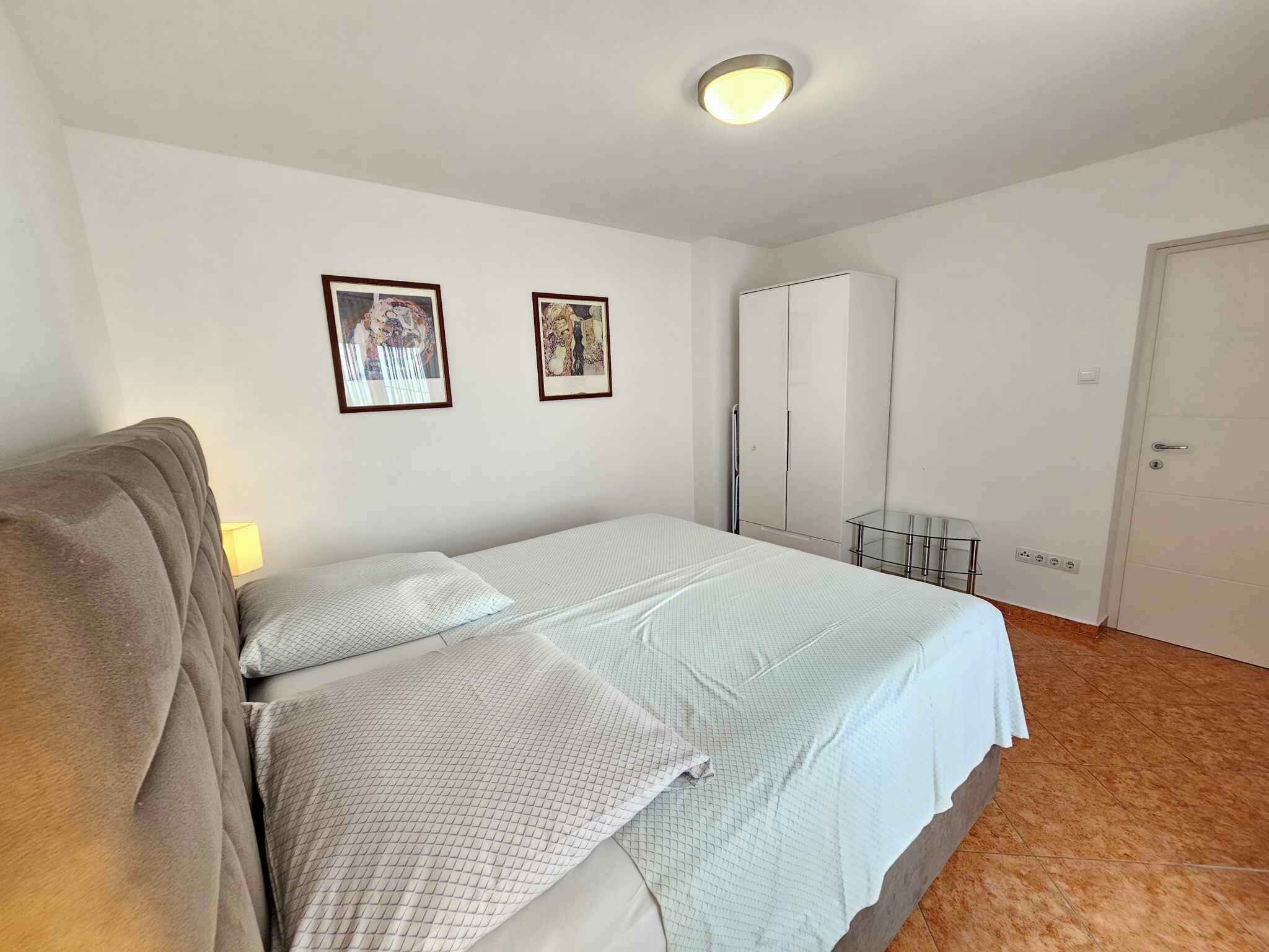 Un dormitorio con una cama, dos cuadros en la pared, un armario y una mesita de vidrio.