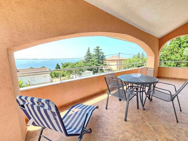 Un balcón con mesa y sillas, con vista al mar y edificios circundantes.