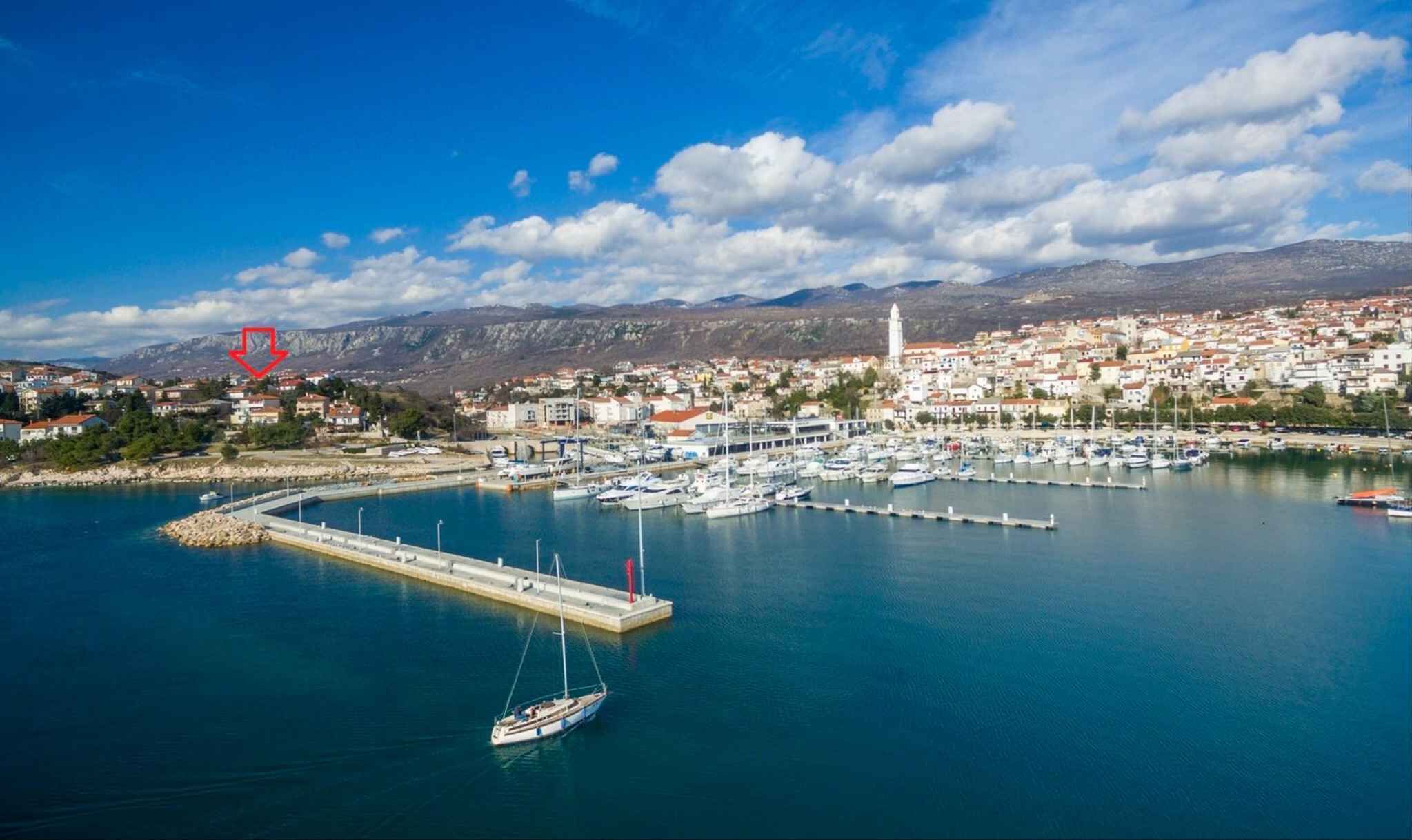 Eine Küstenstadt mit einer Marina, einem markanten Turm und einer gebirgigen Kulisse.