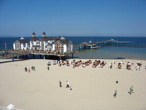 A beach with a pier and a building with multiple windows and a flag.