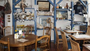 Un restaurante con mesas y sillas de madera, estanterías con botellas y adornos, y una decoración en tonos azules y blancos.
