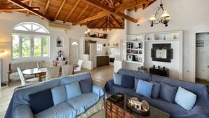 Un vaste espace de vie doté d’un haut plafond en bois, un coin repas avec un banc et une cuisine avec des meubles blancs et une cuisinière.