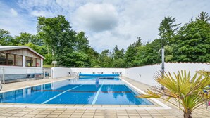 A swimming pool with clear blue water, surrounded by a white wall and a wooden deck.