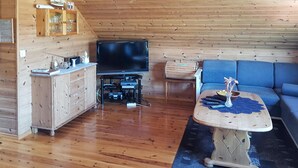 Een gezellige woonkamer met een houten plafond, een televisie, een houten kast, een blauwe bank en een klein tafeltje met een vaas.